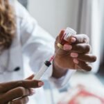 Close-up of a doctor's hands preparing a syringe with a vial, in a clinical setting.