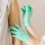 Close-up of gloved hands giving a vaccine injection to a patient's arm.